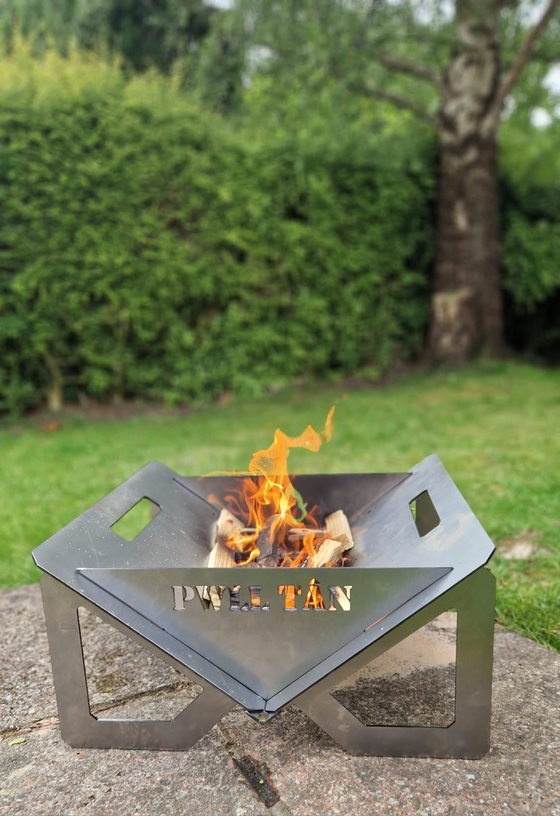Pwll Tân foldable fire pit assembled and burning in a garden setting